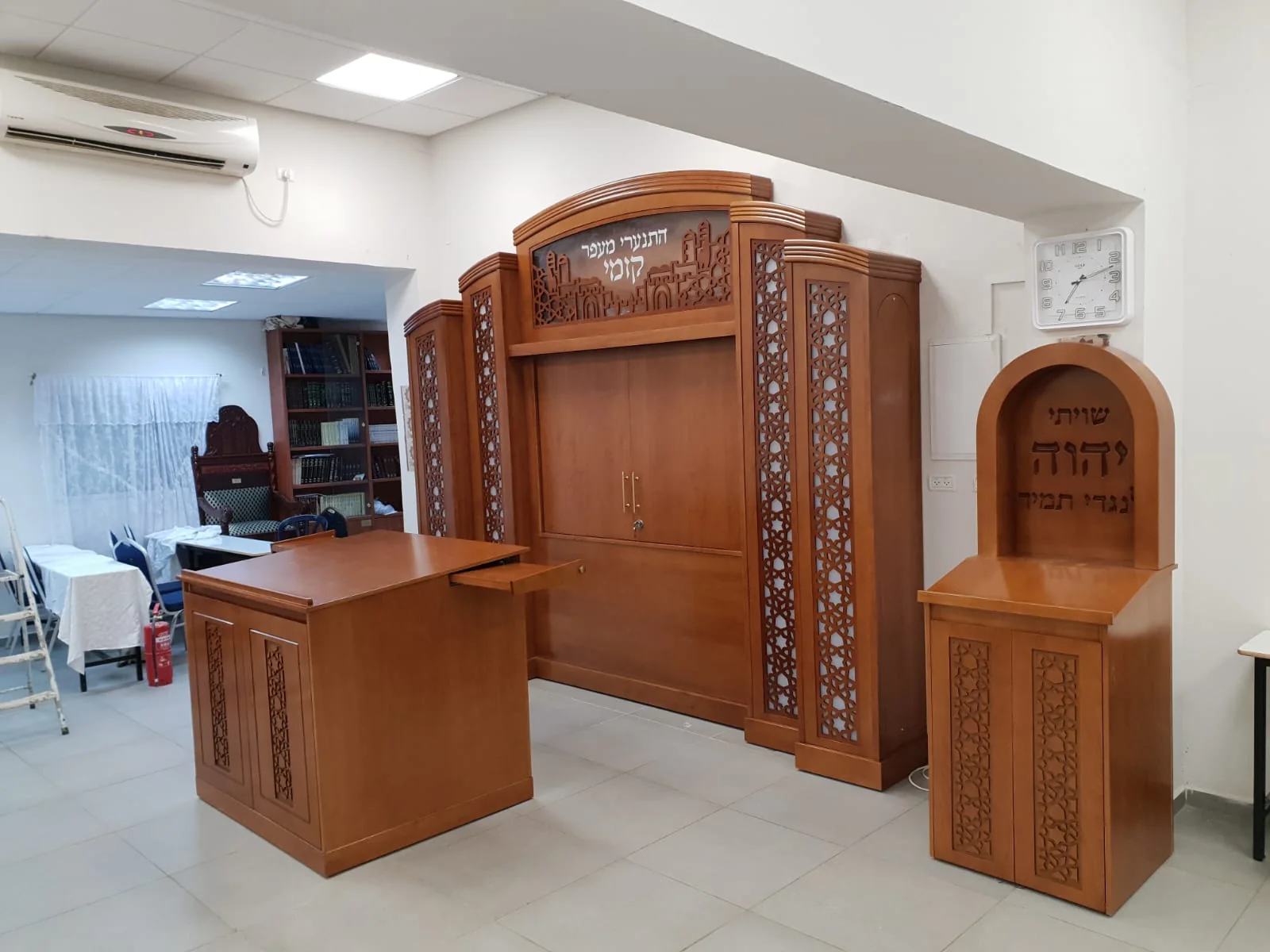 ריהוט בית הכנסת דוסא לאחר ההתקנה: ארון הקודש, התיבה ועמוד התפילה בעץ עם עיטורי מגזרות