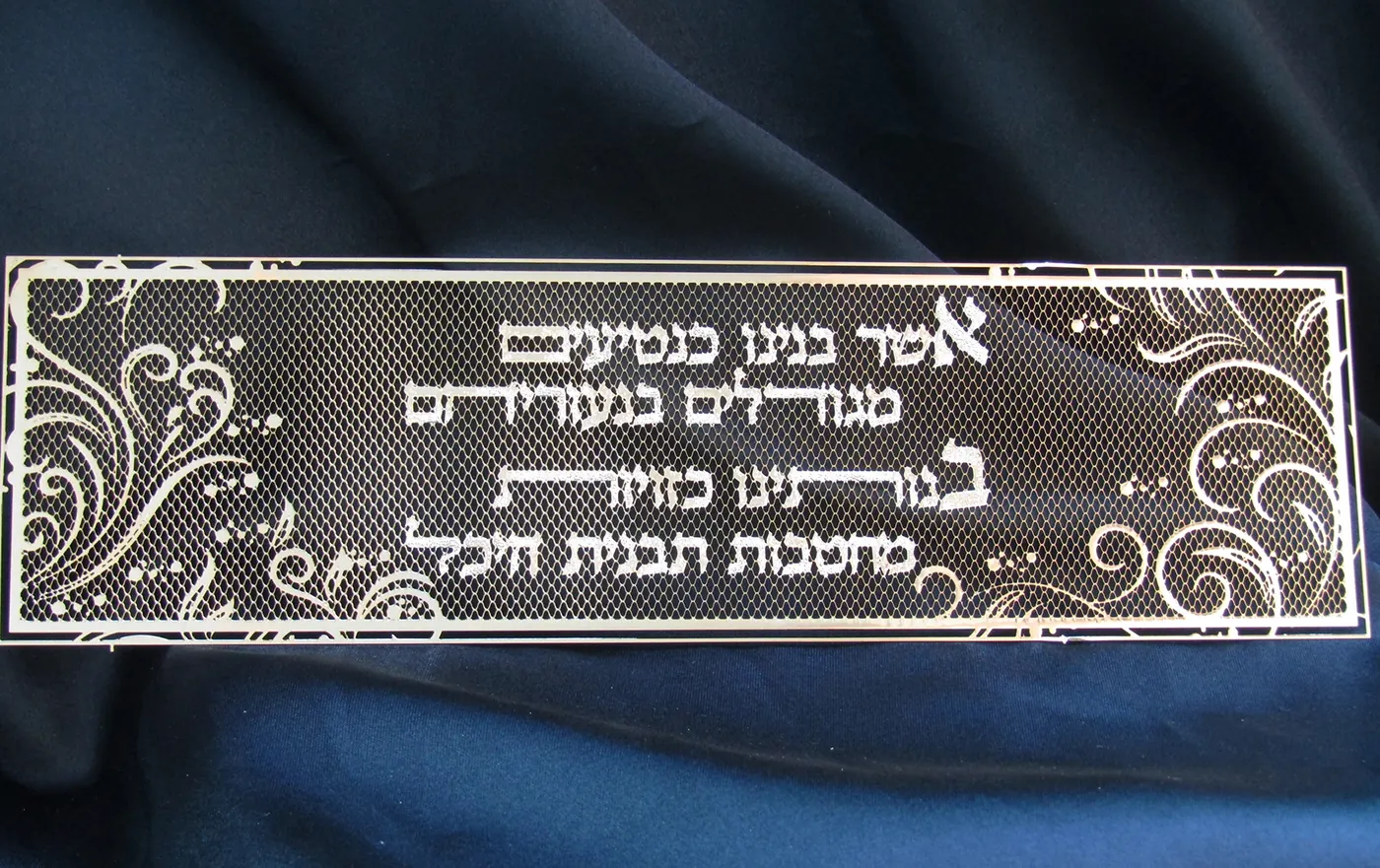 מגזרת מתכת מוזהבת עם הפסוק אשר בנינו כנטיעים ועיטורים מסולסלים, על בד כחול כהה